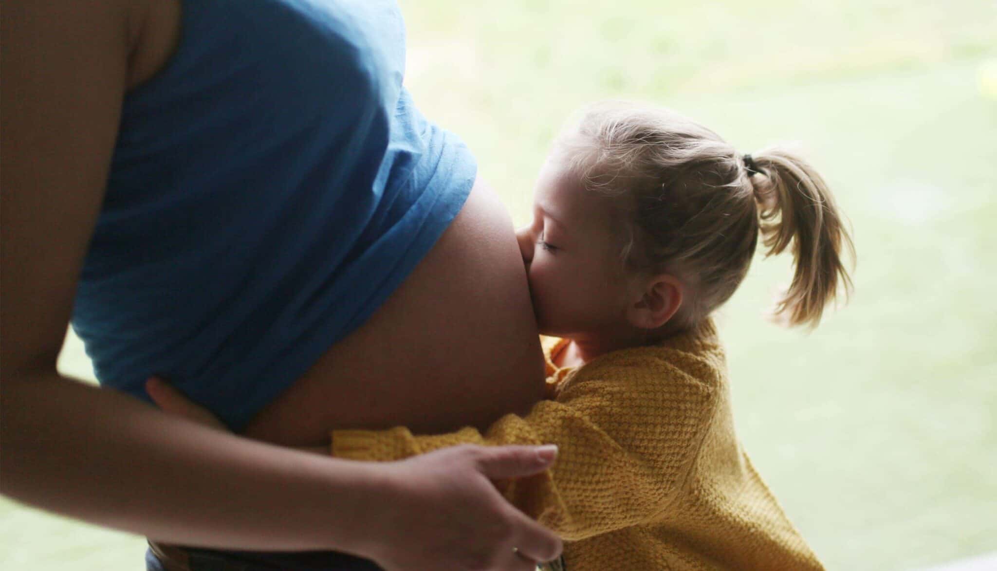 Tochter küsst schwangeren Bauch der Mutter